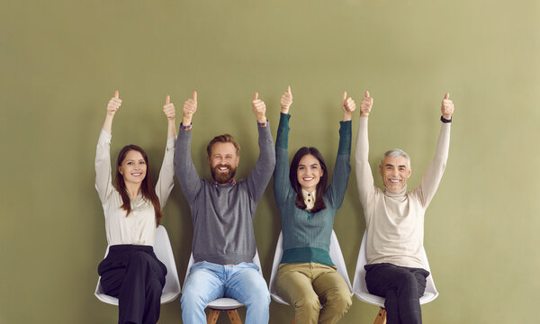 Portrait of four happy satisfied people sitting in row with arms raised and showing thumbs up. Men and women who have been hired or who have received good positions give positive response to hiring.