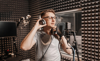 The vocalist sings in the studio in a microphone. Man in headphones writes a podcast, an audiobook....