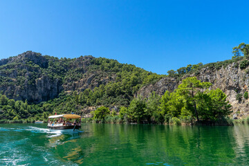 Fototapeta na wymiar Tourist pleasure boat on the Dalyan River, next to the rocks, which contain the Lycian tombs, in Mugla Province located between the districts of Marmaris and Fethiye on the south-west coast of Turkey