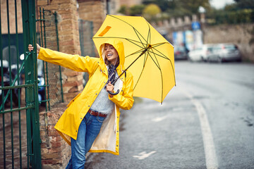 A young girl with yellow raincoat and umbrella is having fun while walking the city on the rain. Walk, rain, city