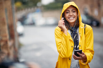 Girl in a yellow raincoat listens to music in the rain