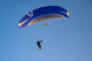 Silhouette of a man on a paraglider flying in the blue sky.
