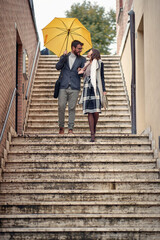 A young couple in love which is descending the stairs in the city during a rainy day. Walk, rain,...