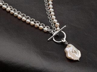 Fototapeta na wymiar Neklace and pendant of baroque pearls on black leather background