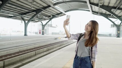 Beautiful young Asian woman backpacker wearing using smartphone for taking selfie on platform at red line train station.