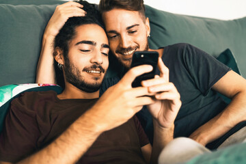 Male gay couple using smartphone in the bedroom - homosexual LGBT concept -