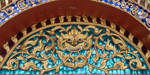 Detail of gilded stucco on glass mosaic representing Kala aka kirtimukha, a guardian and protector deity above entrance of Wat Chiang Man vihara, the oldest buddhist temple in Chiang Mai, Thailand
