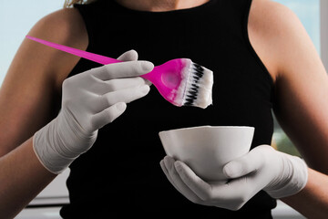 woman in white rubber protective gloves holding a brush in her hands and stirring hair dye close-up colorist hair care at home hair mask