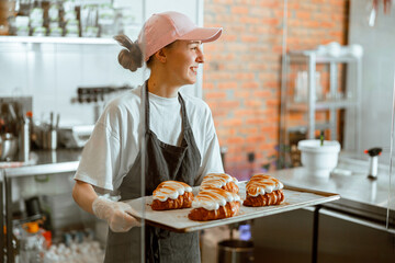 Pretty woman baker holds beautiful croissants with burnt albumenous cream in shop - obrazy, fototapety, plakaty