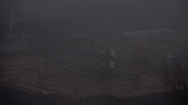 Workers on top of construction site in thick autumn morning fog