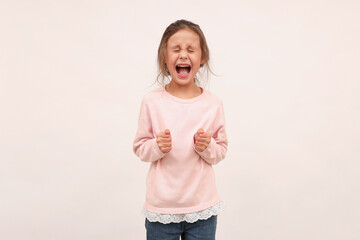 An angry little girl loses her temper, argues, complains, looks angry and dissatisfied, screams in rage, worries, stands on a white background.