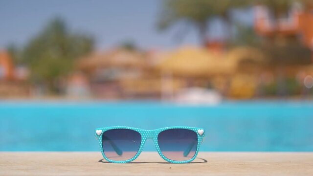Closeup of blue sunglasses on swimming pool side at tropical resort on warm sunny day. Summer vacation concept