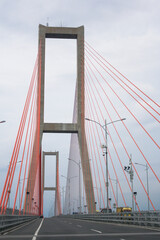 Scene of the famous Suramadu Bridge and its red suspension steel cables with lamp post on road and cloudy sky background.