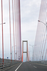 Scene of the famous Suramadu Bridge and its red suspension steel cables with lamp post on road and cloudy sky background. 