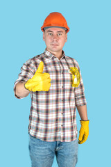 A construction worker in an orange helmet and gloves shows a thumbs up. Vertical photo