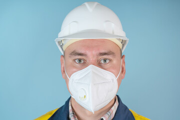 Large portrait of a man, architect, worker, in a white helmet and protective mask on a blue background