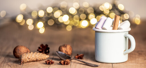 Obraz na płótnie Canvas christmas banner with cup with hot chocolate and marshmallows on with cinnamon sticks and fir xmas tree branches with beautiful bokeh lights. New year celebration