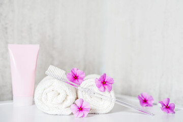 Fototapeta na wymiar Toothbrush, toothpaste and white towels, pink flowers with copy space. Aromatherapy and Oral care, body hygiene and morning daily routines.
