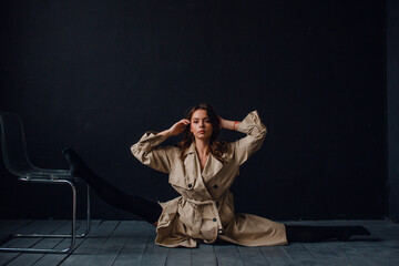 young beautiful girl in the studio on a black background, she is wearing a trench coat and black lingerie
