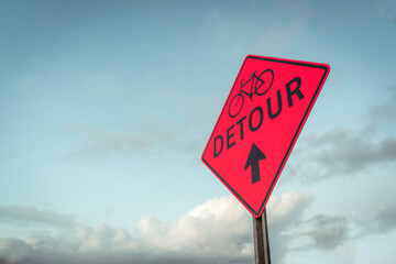Detour bike and arrow sign in front of clouds and blue sky