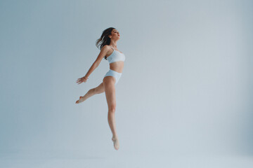 girl gymnast, in a white uniform, panties and top, in the studio on a white background shows...