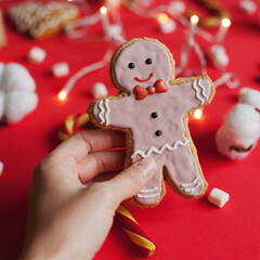 Hand holding christmas gingerbread man cookie on red festive background closeup