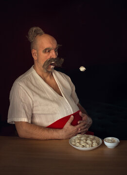 Funny man dressed like cossack is eating flying russian dumplings. Image with selective focus and toning