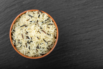 Wild rice in a clay bowl against a black background.