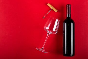 Fototapeta premium Bottle of red wine and an empty wine glass with a corkscrew next to it. Composition on a red background. Romantic mood. Space for text.