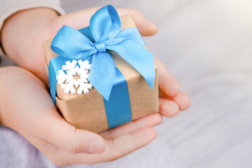 Close-up of hands holding a small gift. A gift wrapped in a blue ribbon and decorated with a snowflake. 