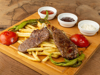 french fries meatballs pepper tomatoes and sauces on black plate on wood