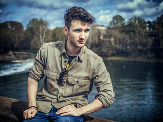 Three-quarter length of young man standing beside picturesque river in Turin, Italy
