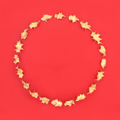 Gold holly leaf wreath for Christmas on red background. Festive minimal symbol for the holiday season. Flat lay, top view, copy space.