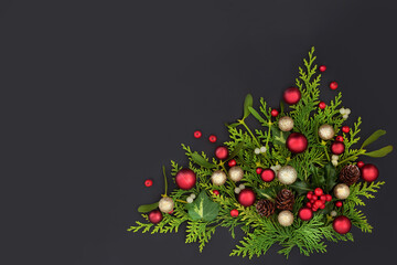 Festive Christmas nature abstract background with red, gold baubles, holly, cedar, mistletoe, acorns, ivy leaves with loose red berries on dark grey. Top view, copy space.