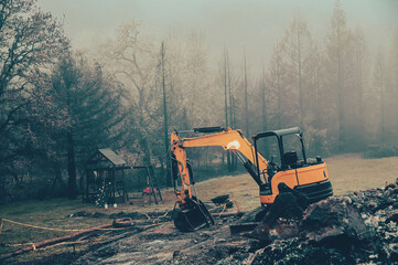 Small excavator clears the area after a fire in the fog in the evening
