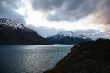Obraz premium Paisaje de un río en entre las montañas nevadas con un cielo nublado en un atardecer