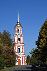 Fototapeta na wymiar The brick bell tower of the ancient Orthodox Cathedral of the Resurrection of Christ stands surrounded by trees in the ancient city of Staraya Russa, Novgorod region. Ancient Russian architecture of 