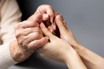 Mother and daughter holding hands. Close-up. Gray background. The concept of caring for the elderly...