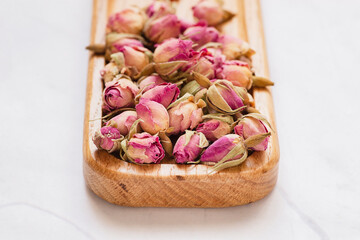 Dry buds of a tea rose on wooden plate. Filler for herbal tea. Decor for natural soap and candles. Flowers composition in flat lay style
