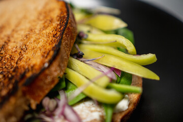 Sandwich of toasted bread and stuffed with fresh organic vegetables and herbs. Yellow and green peppers cut into pieces, onions, green leaves and microgreens. Delicious nutritious breakfast. Dish.
