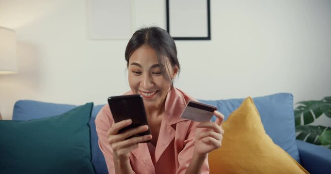 Closeup young asia lady use cellphone order online shopping product and paying bill with credit card sit on couch in living room at house, Quarantine activity, Fun activity for coronavirus prevention.