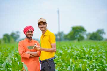 Young indian banker or agronomist showing some detail to farmers in smartphone at agriculture field.