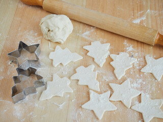 Uncooked biscuits cut with metal molds on a wooden table, sprinkled with flour. Making homemade cookies for Christmas