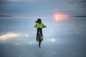 Boy riding a bike at sunset over salt lake