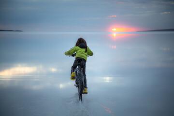 Boy riding a bike at sunset over salt lake