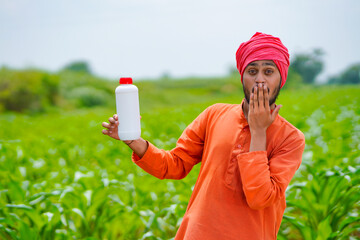Young indian farmer showing liquid fertilizer bottle at agriculture field.