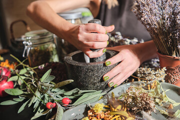 The girl grinds dry herbs in a mortar. Preparation of a mixture of dried herbs for making tea,...