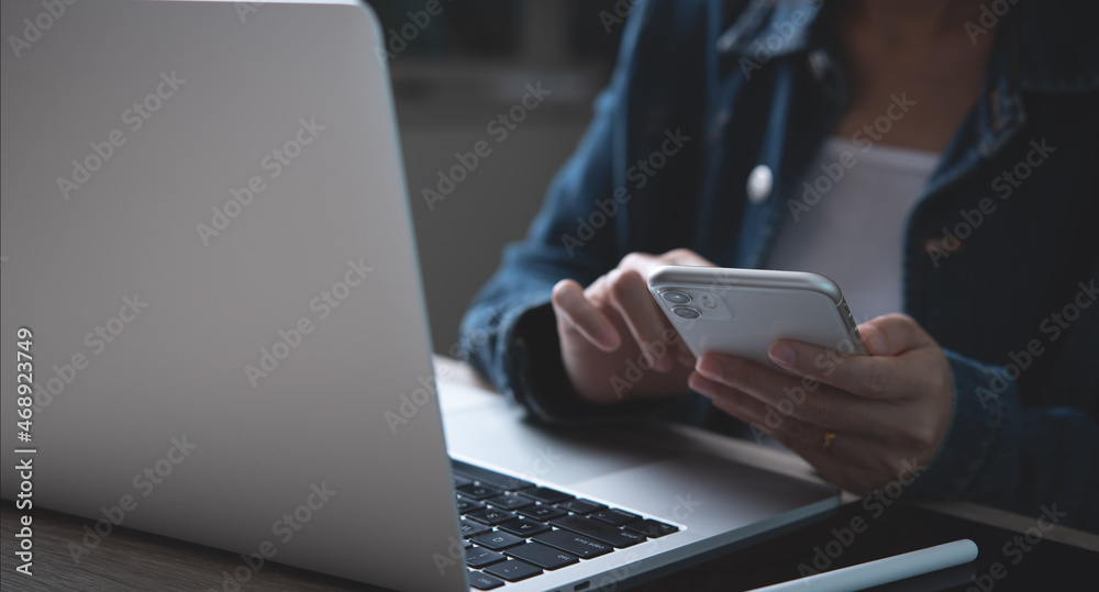 Wall mural closeup of business woman using mobile smart phone and working on laptop computer on office table at