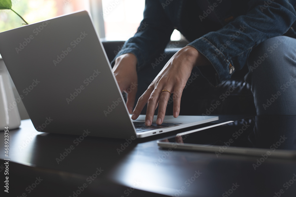 Wall mural young casual business woman, freelancer in blue jeans and sweater sitting on sofa working and typing