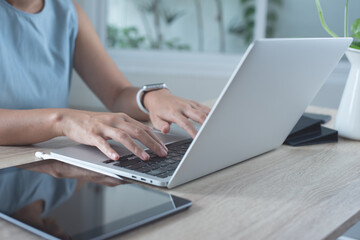 Closeup of casual business woman typing, working on laptop computer, surfing the internet with digital tablet on office table at her workplace